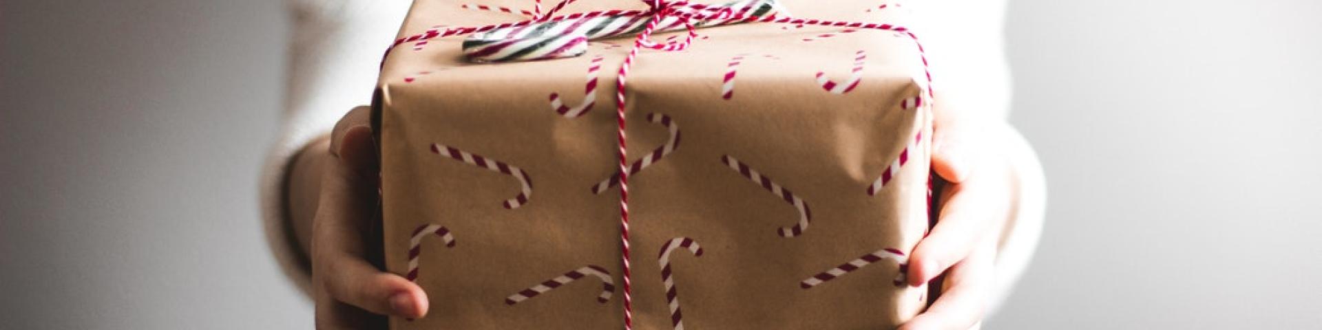 A teenage girl holding out a gift with candy cane wrapping paper