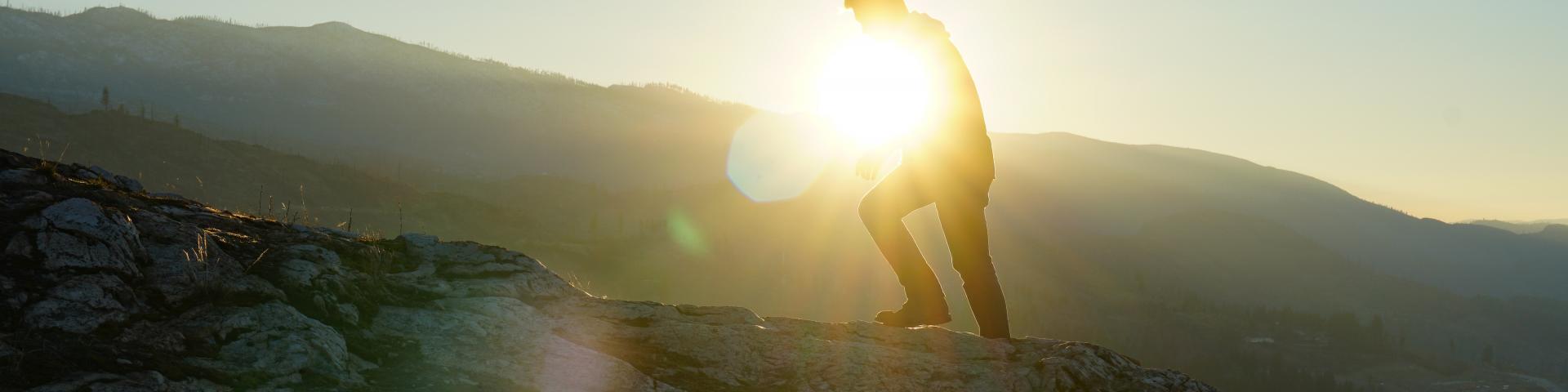 The silhouette of a person climbing on a mountain with the sun in the background 
