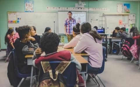 Students at their desks watching their teacher teach