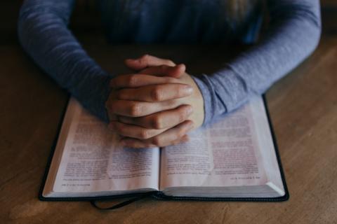 A person's hands folded in prayer on top of a bible