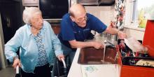 Picture of a husband helping his wife in the kitchen. Wife has a walker. 
