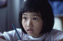  Child sitting with a pen at a desk looking up