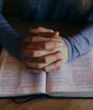 Two hands folded in prayer with a bible 